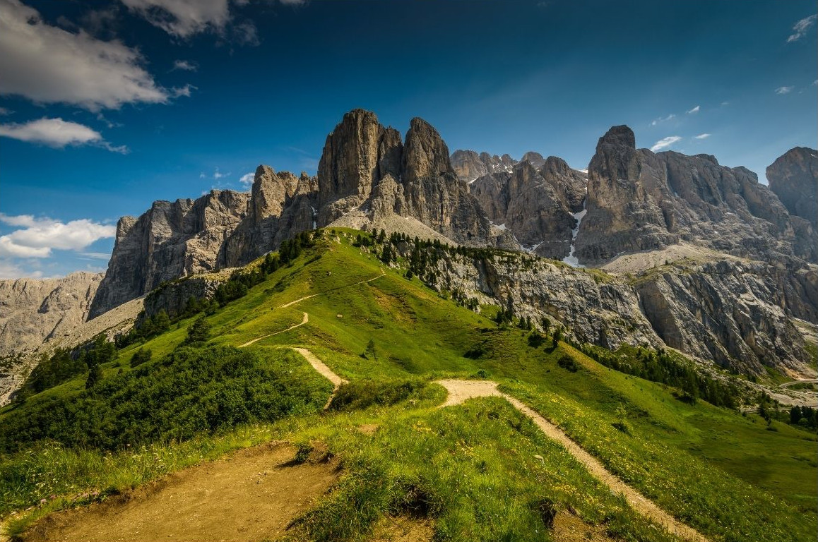 Vandringsled över gröna kullar med Dolomiterna som reser sig upp i bakgrunden