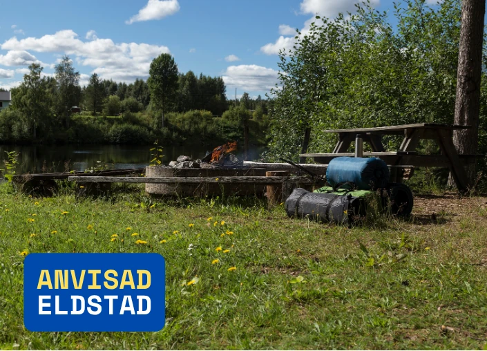 Gjort upp eld i anvisad eldstad, bredvid grillplatsen ligger stora tältdukar redo att sättas upp för tältcamping